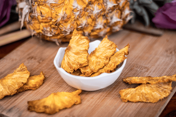 Bol d’ananas séchés avec un ananas entier en arrière-plan pour une collation saine et énergétique